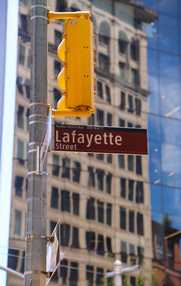 A Lafayette Street sign and traffic light against a glass tower