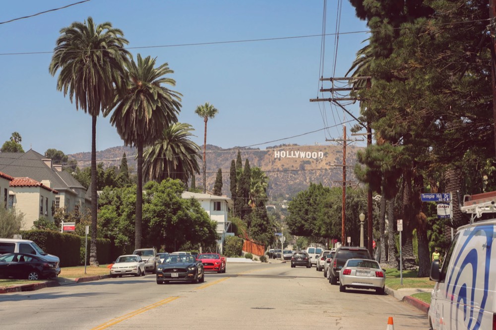 A palm-lined Los Angeles street with the Hollywood sign in the distance